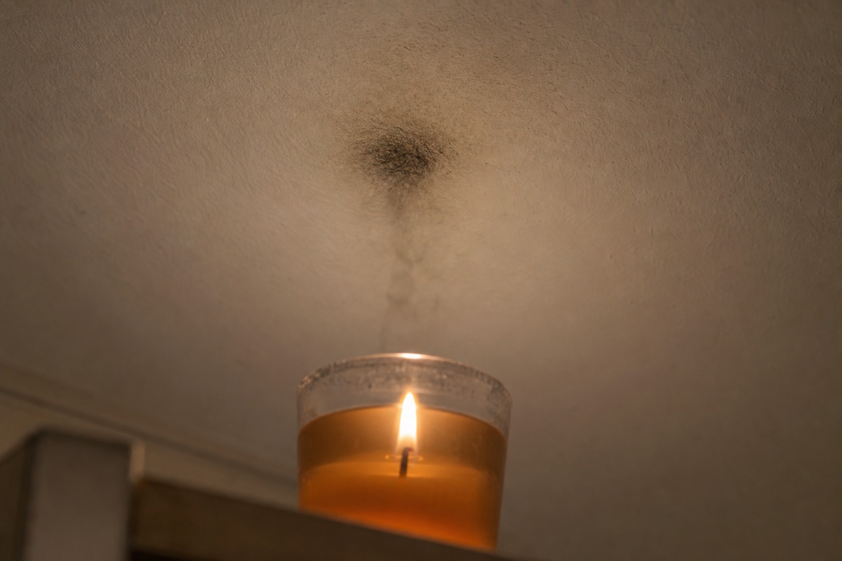 Urmă închisă de funingine pe tavanul alb, chiar deasupra unei lumânări gel care arde într-un pahar de sticlă